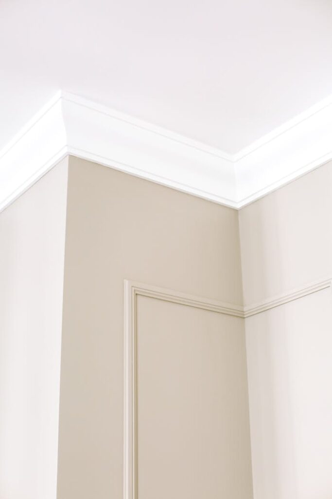 Close-up of intricate ceiling moulding and beige walls with minimalist design, showcasing home renovation details.