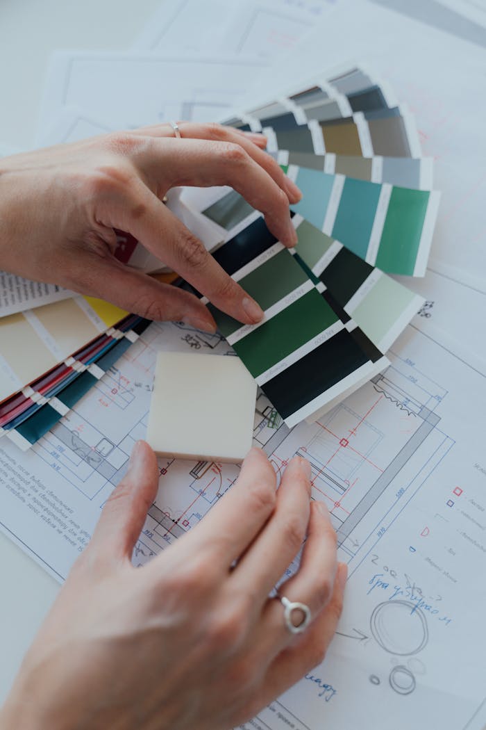 Home Hands selecting color samples over architectural plans for interior design.